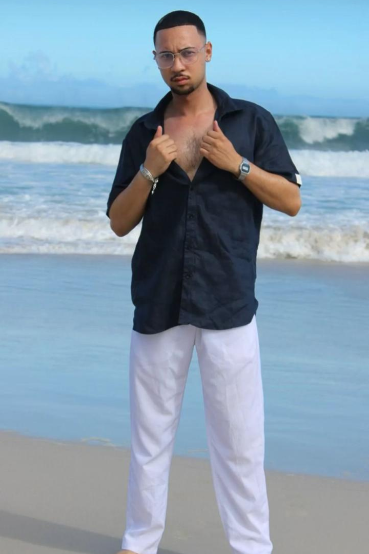 Man standing on a beach wearing a navy shirt and white pants with a watch.