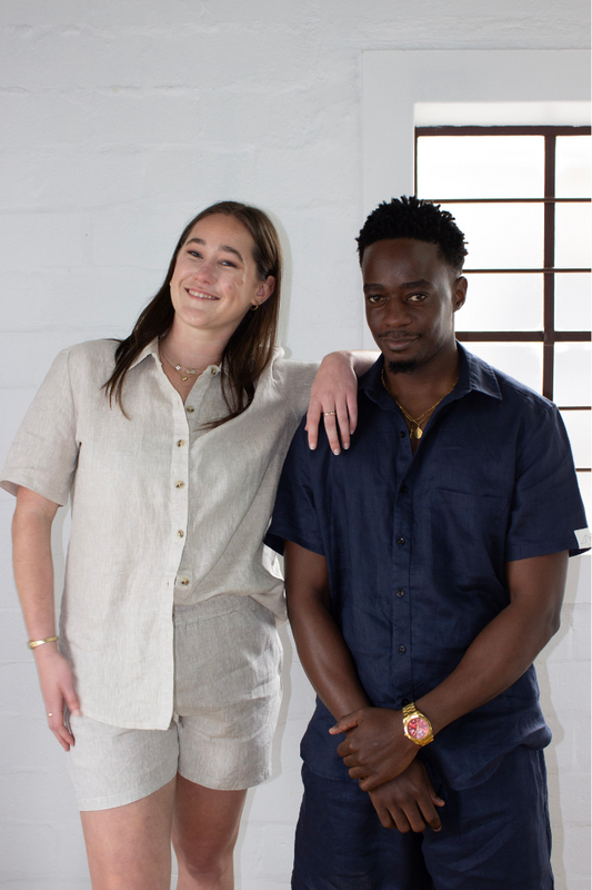 Two people standing close together against a white wall in linen clothing.
