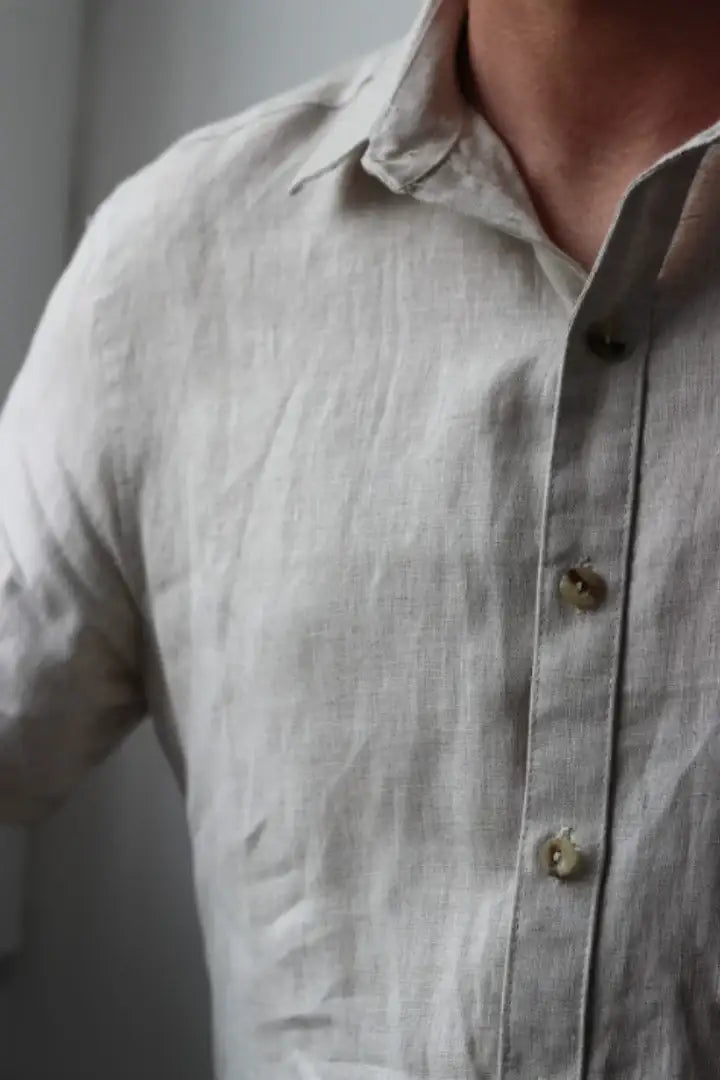 Close-up of a light gray linen shirt with buttons on a neutral background